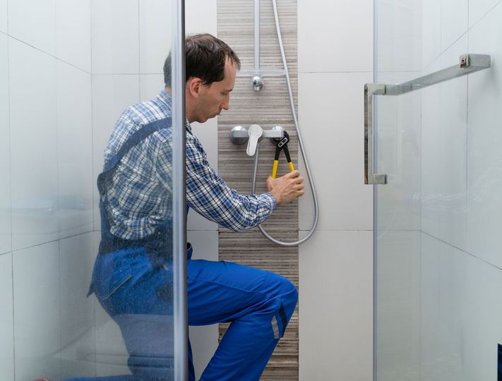A plumber is fixing a shower head in a bathroom.