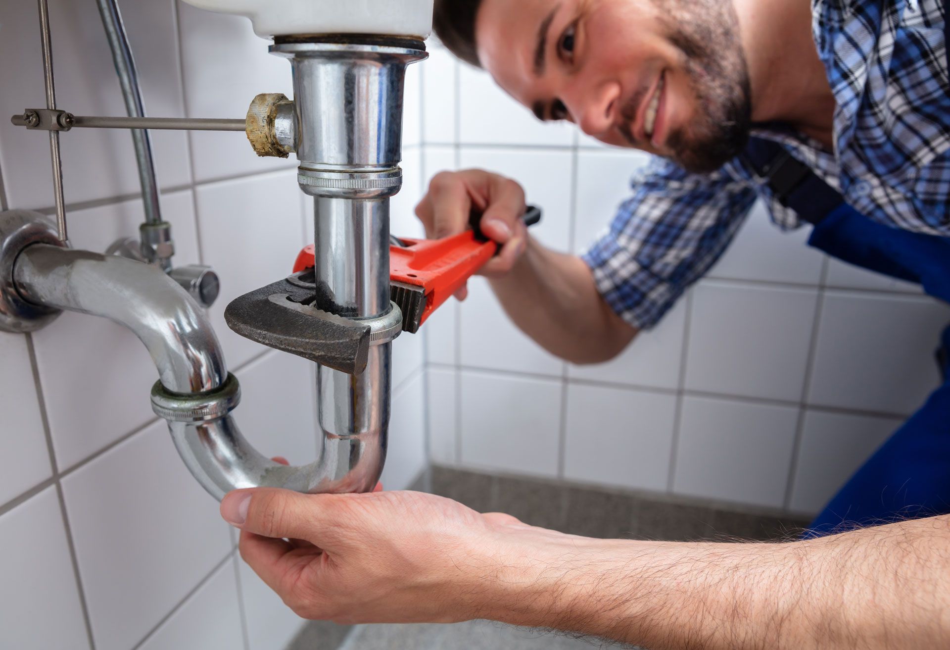 A man is fixing a sink pipe with a wrench in a bathroom.