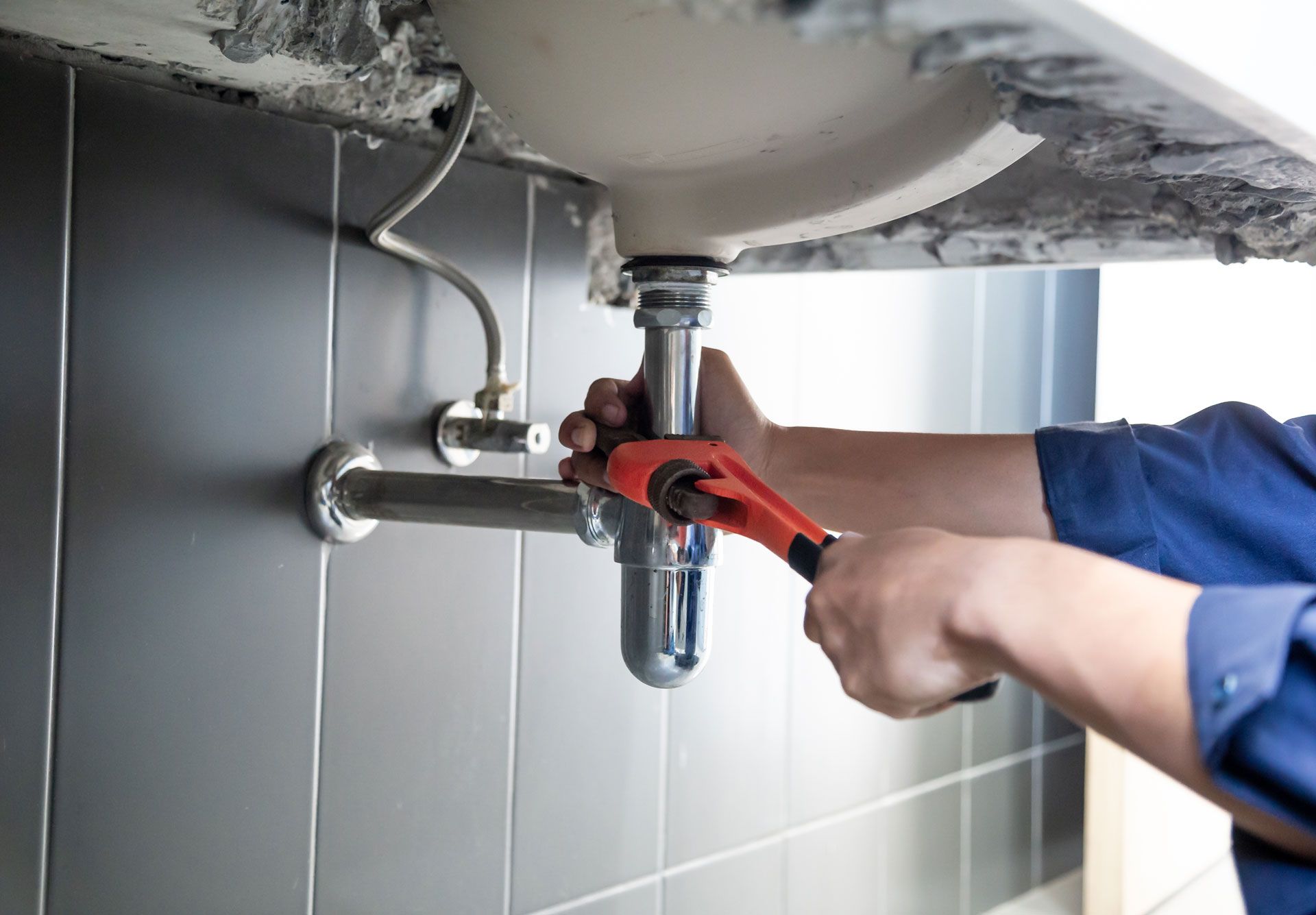 A plumber is fixing a sink with a wrench.