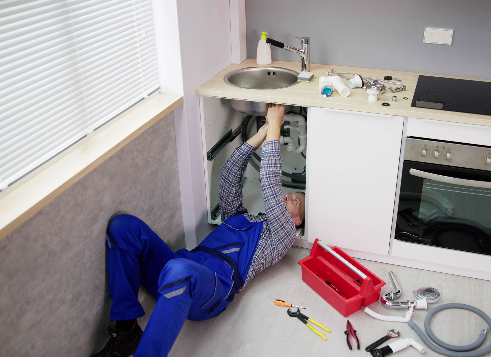 A man is laying on the floor fixing a sink in a kitchen.