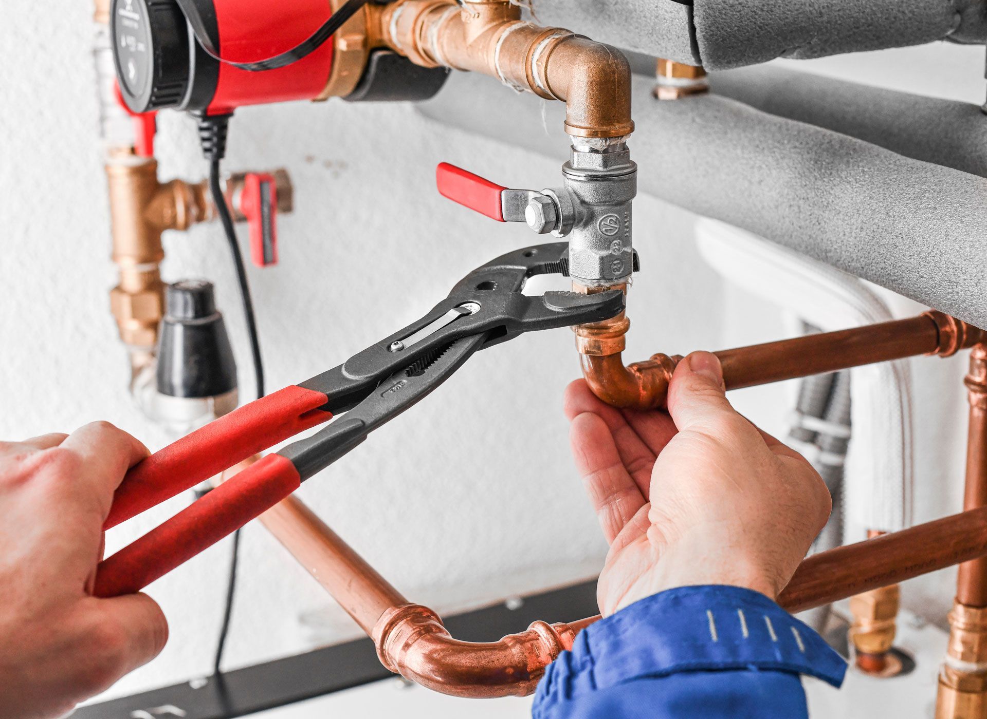 A plumber is fixing a pipe with a pair of pliers.