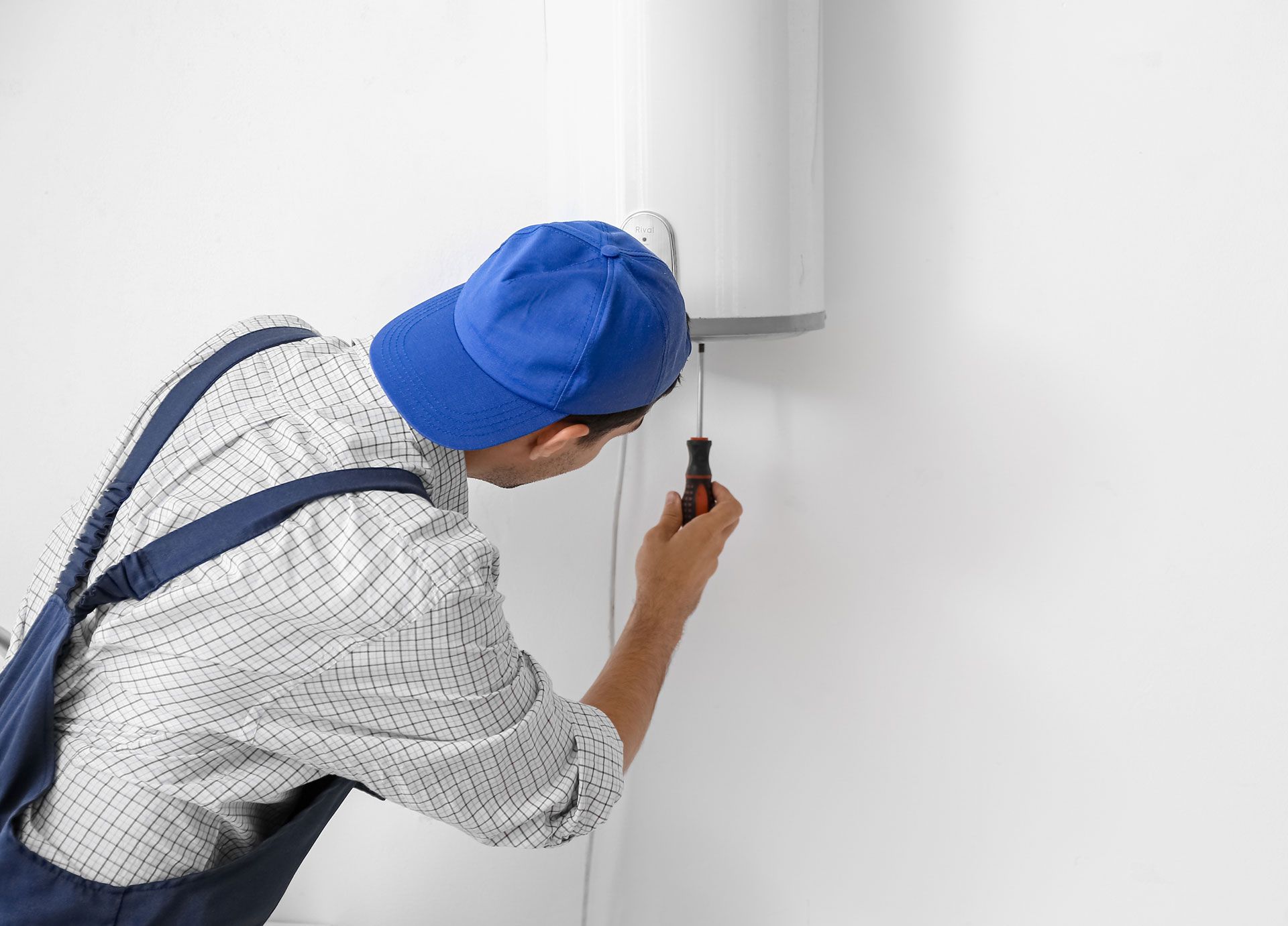 A man is fixing a water heater on a wall with a screwdriver.