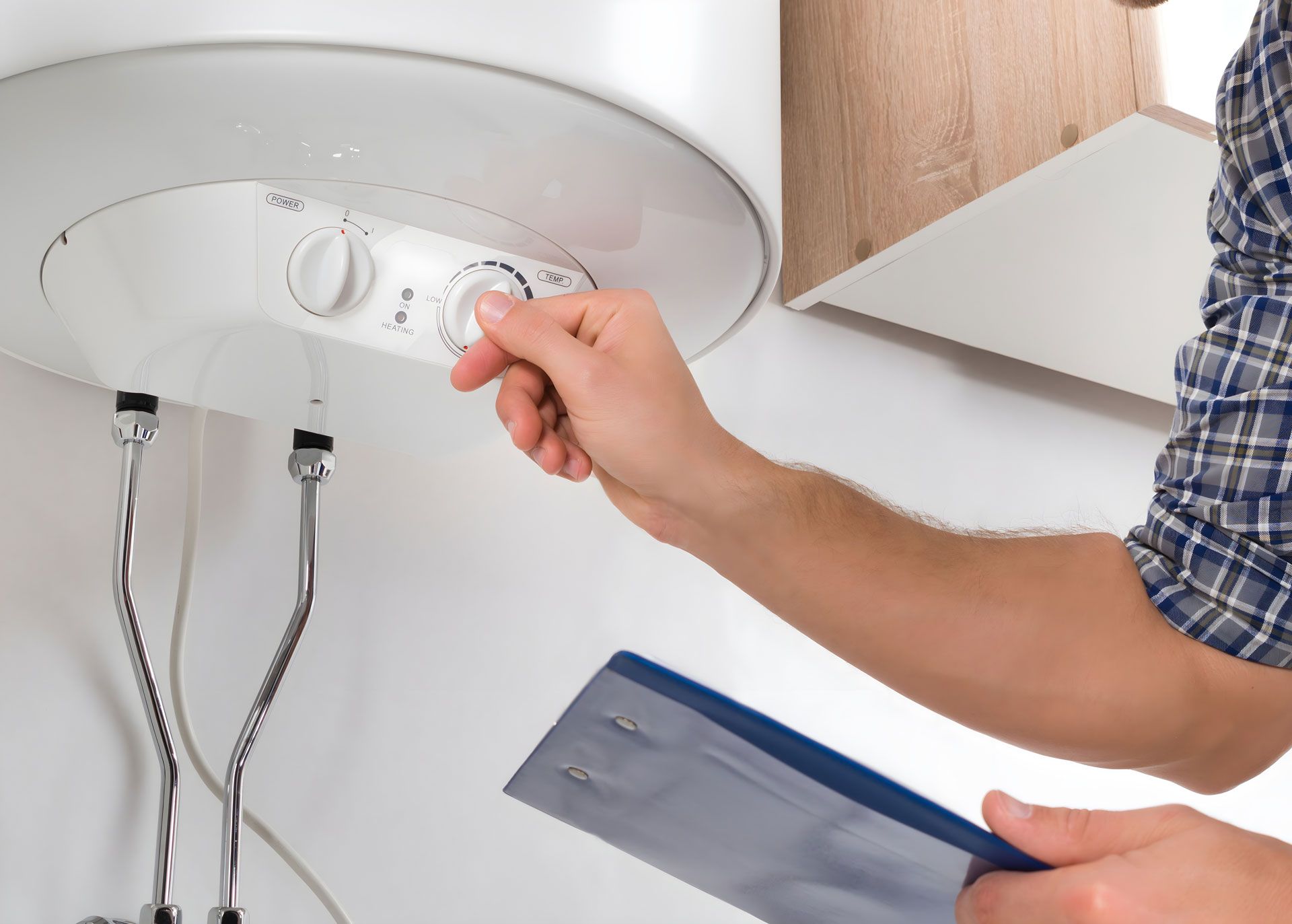 A man is adjusting a water heater while holding a clipboard.
