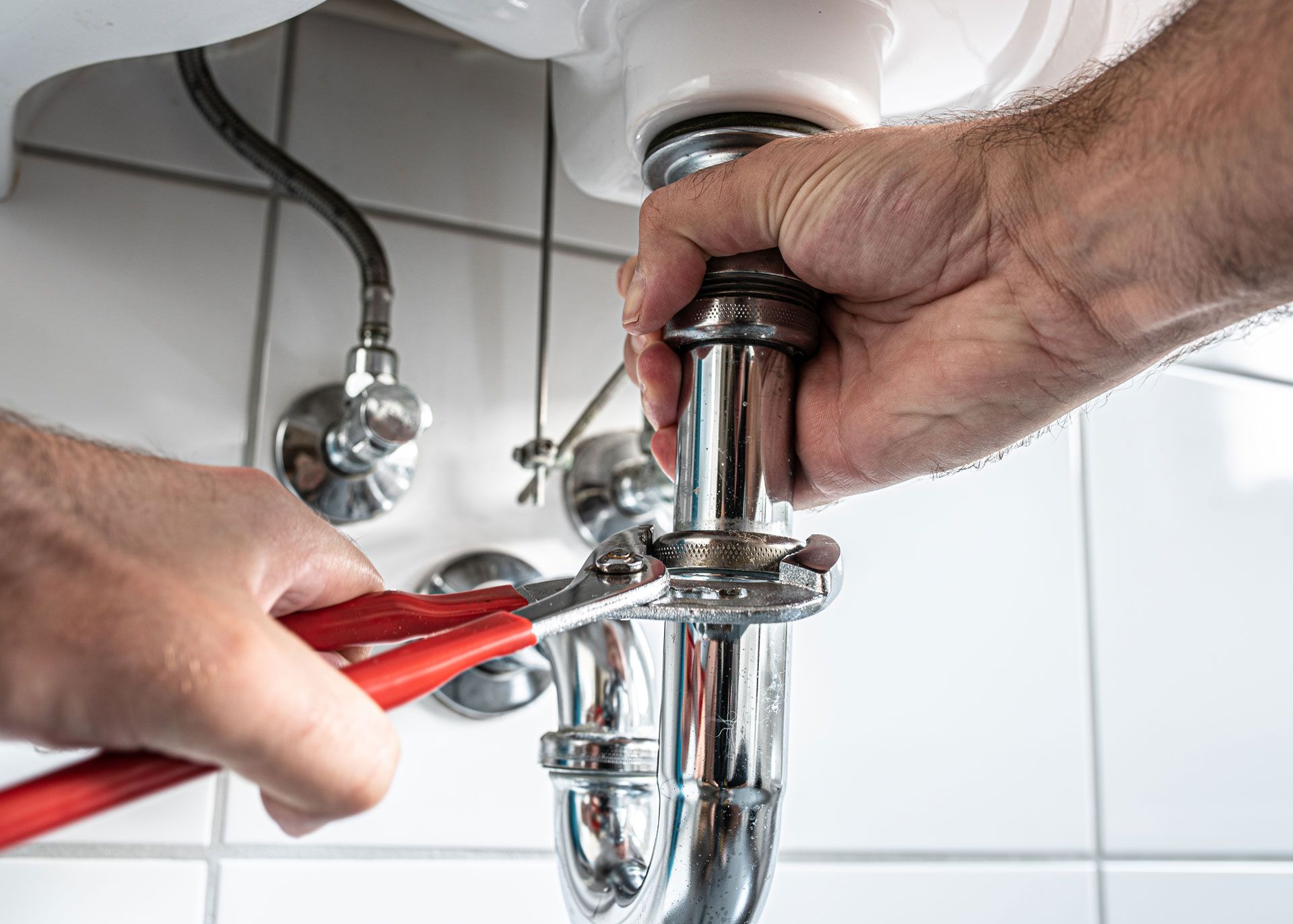 A plumber is fixing a sink pipe with a wrench.