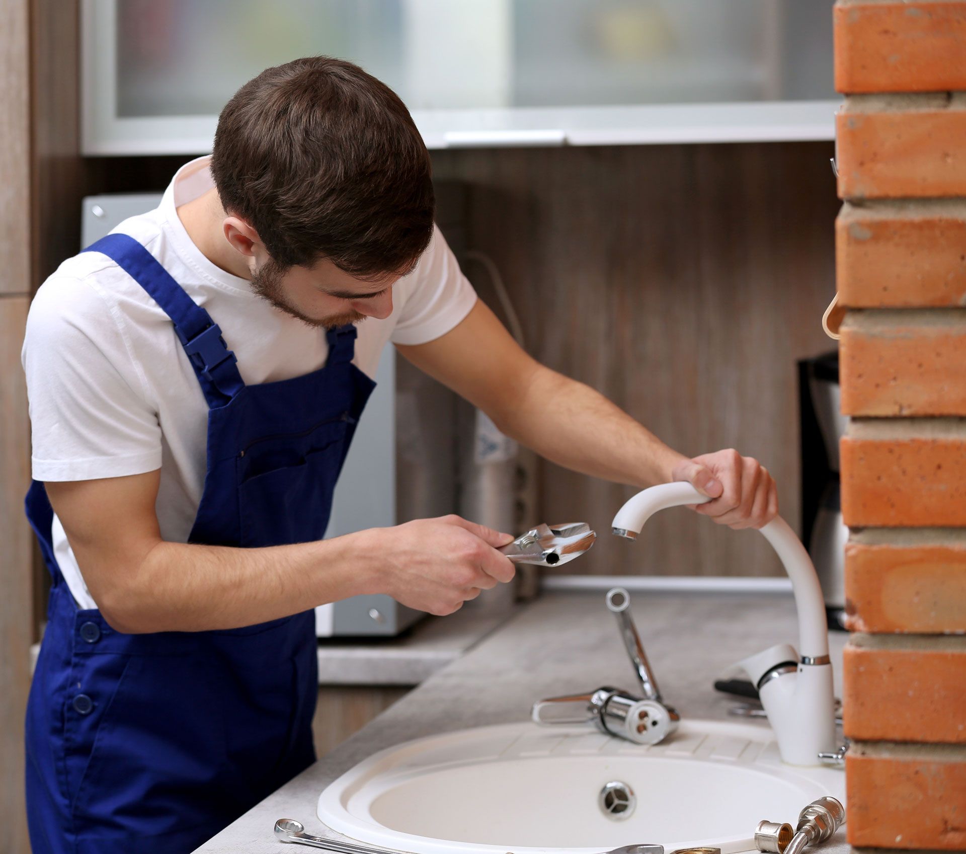 A man is fixing a sink with a wrench.