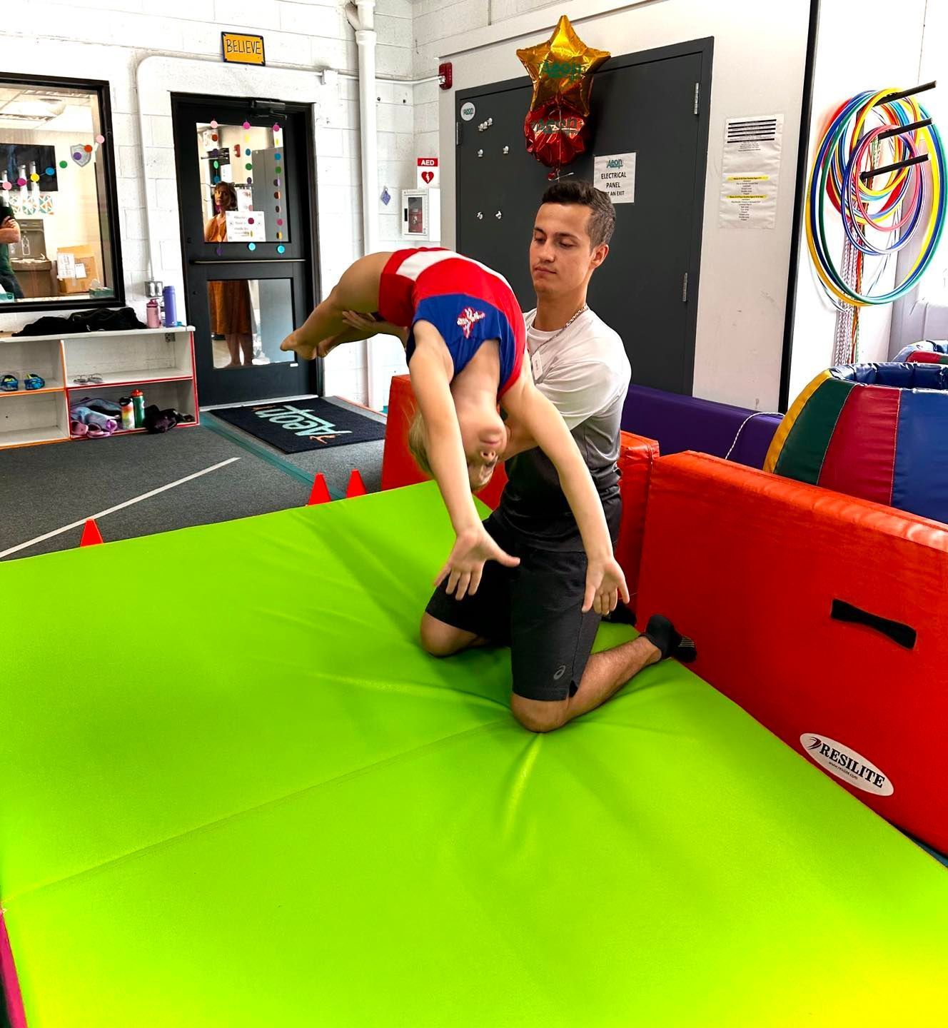 A gymnast in a purple leotard is standing on a balance beam