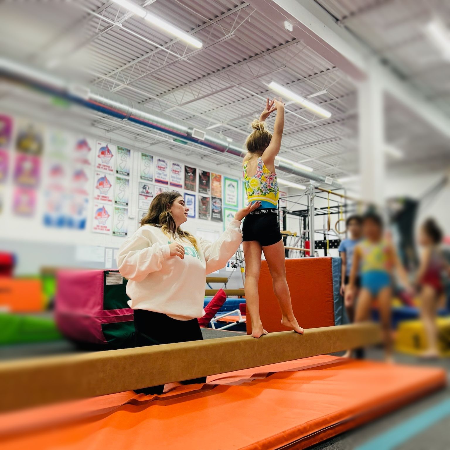 A woman is helping a young girl balance on a balance beam