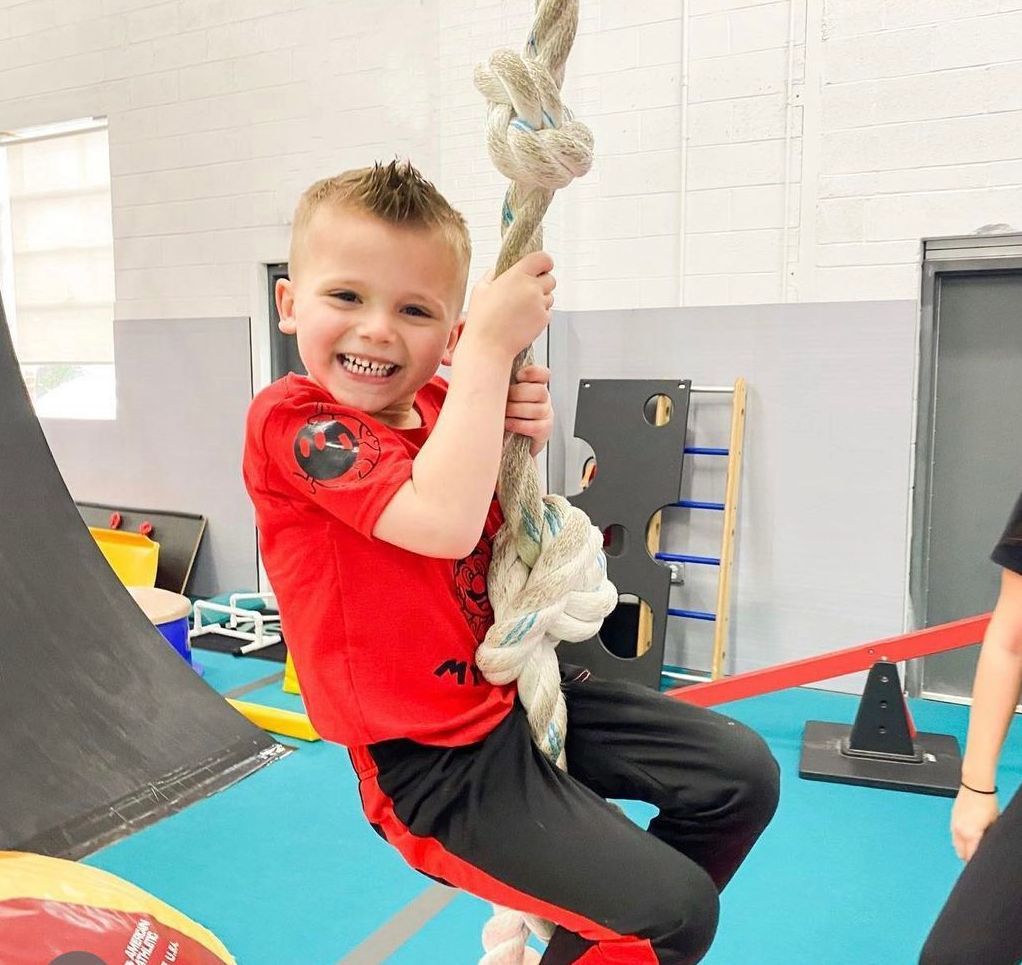 A young boy is swinging on a rope in a gym.