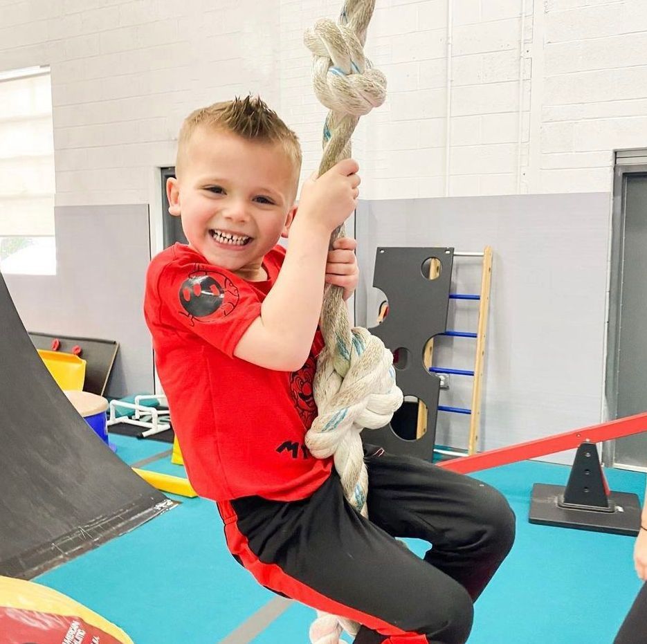 A young boy is sitting on a rope swing and smiling