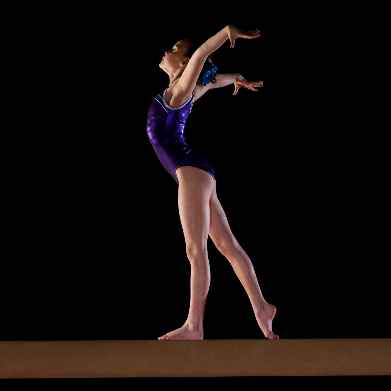 A gymnast in a purple leotard is standing on a balance beam