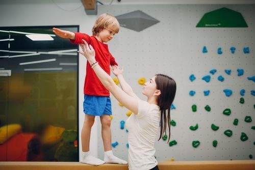 A woman is helping a young boy balance on a balance beam.