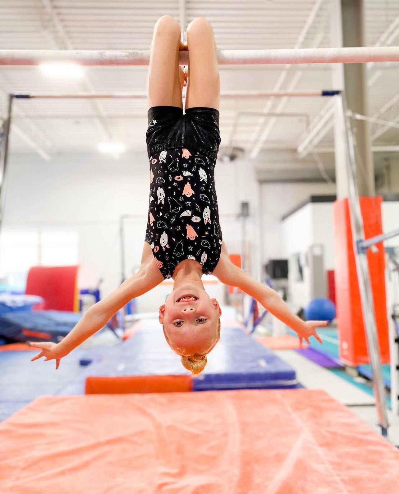 A young girl is doing a handstand on a bar in a gym.