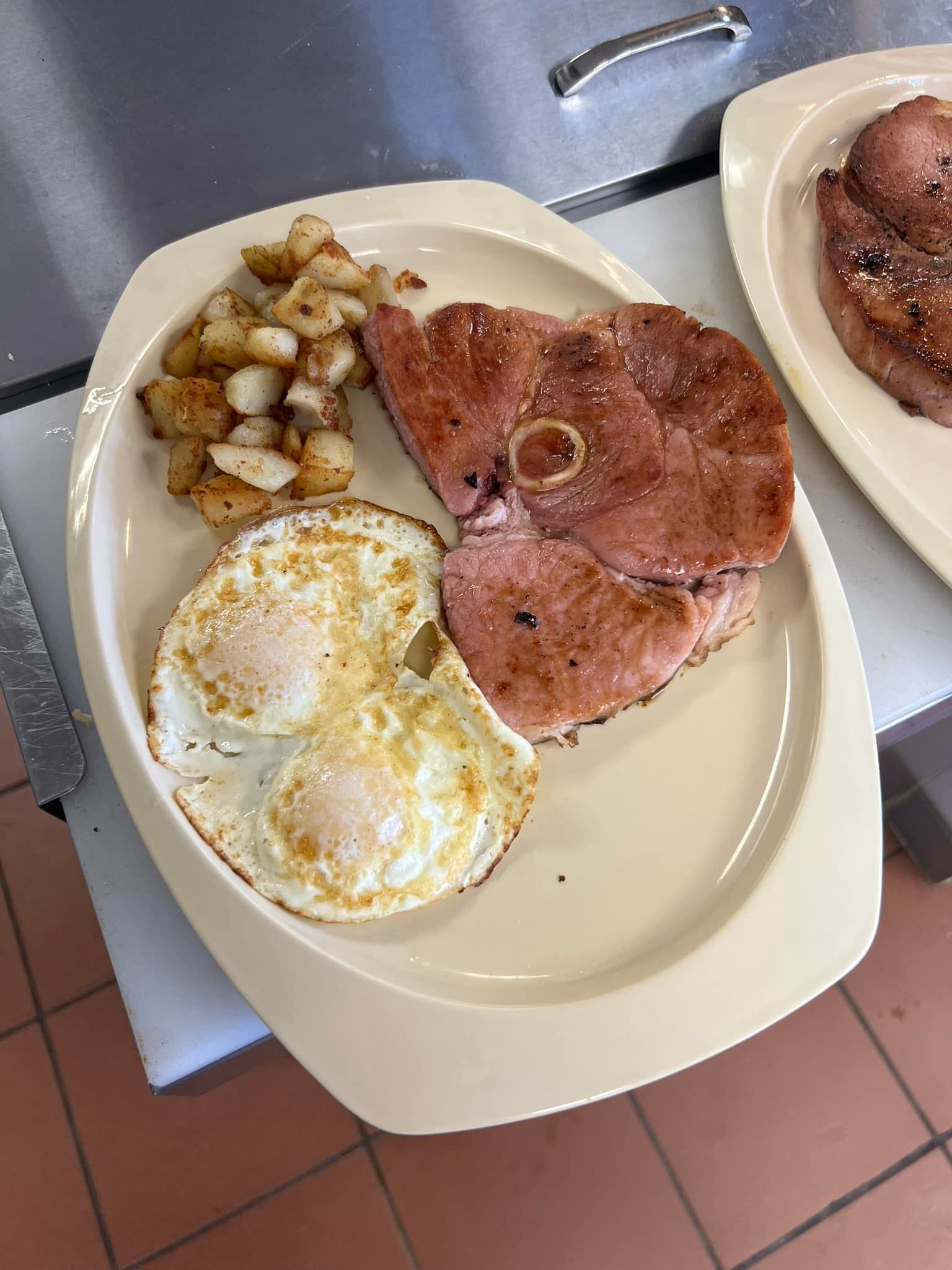 Plate with two fried eggs, sliced ham, and potatoes on a cafeteria tray.