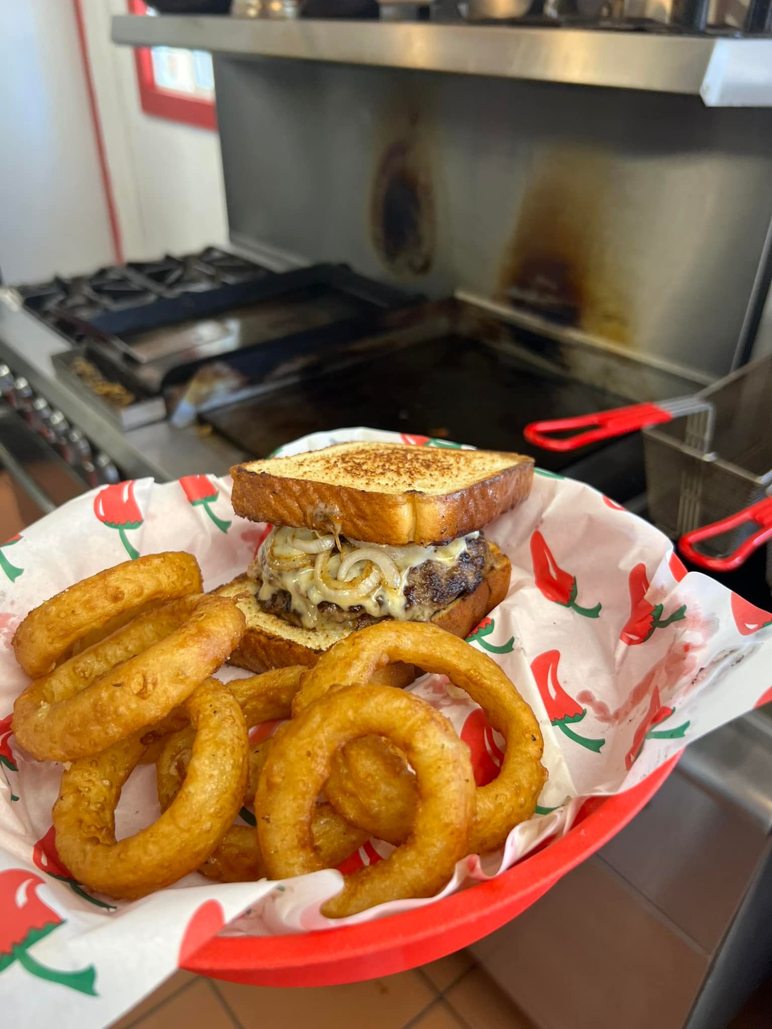 Burger and onion rings in a red basket, with a stovetop in the background.