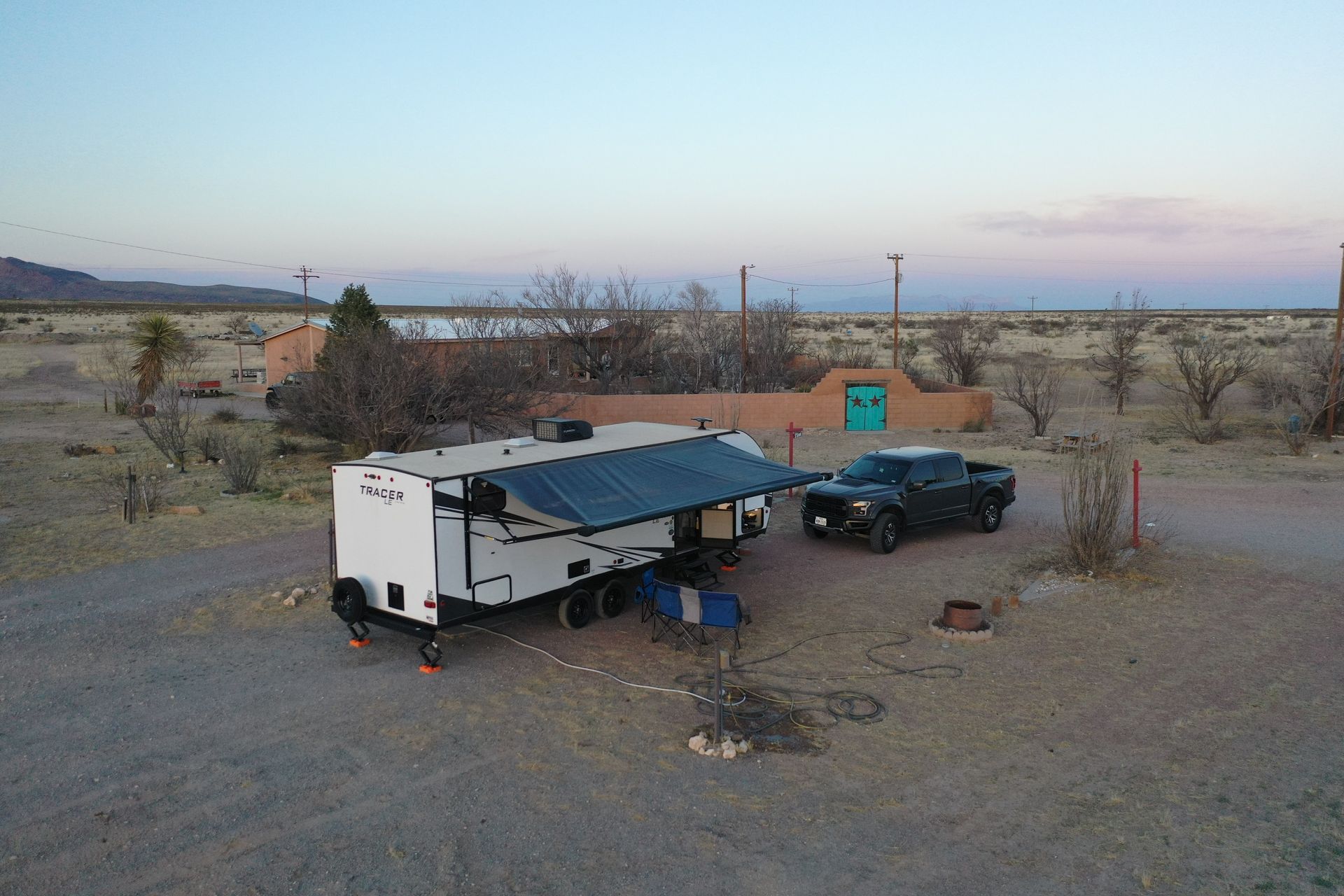 Camper trailer and black SUV parked in a barren desert campsite at dusk