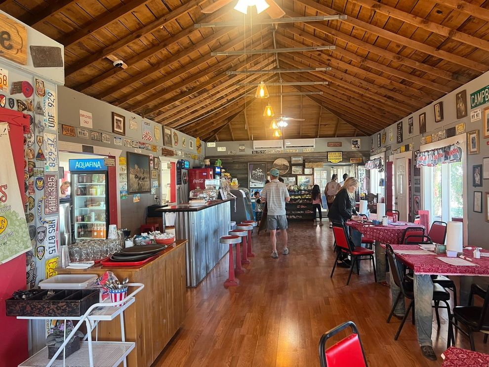 Long rustic dining hall with wooden ceiling, red chairs, and a few people near the back.