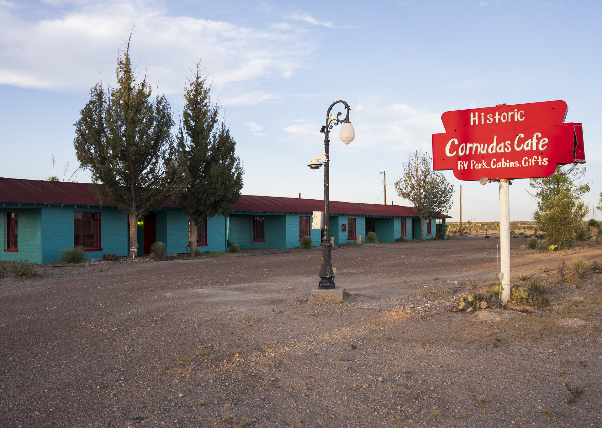 Historic Canada Café building with turquoise walls and red sign along a gravel roadside at sunset