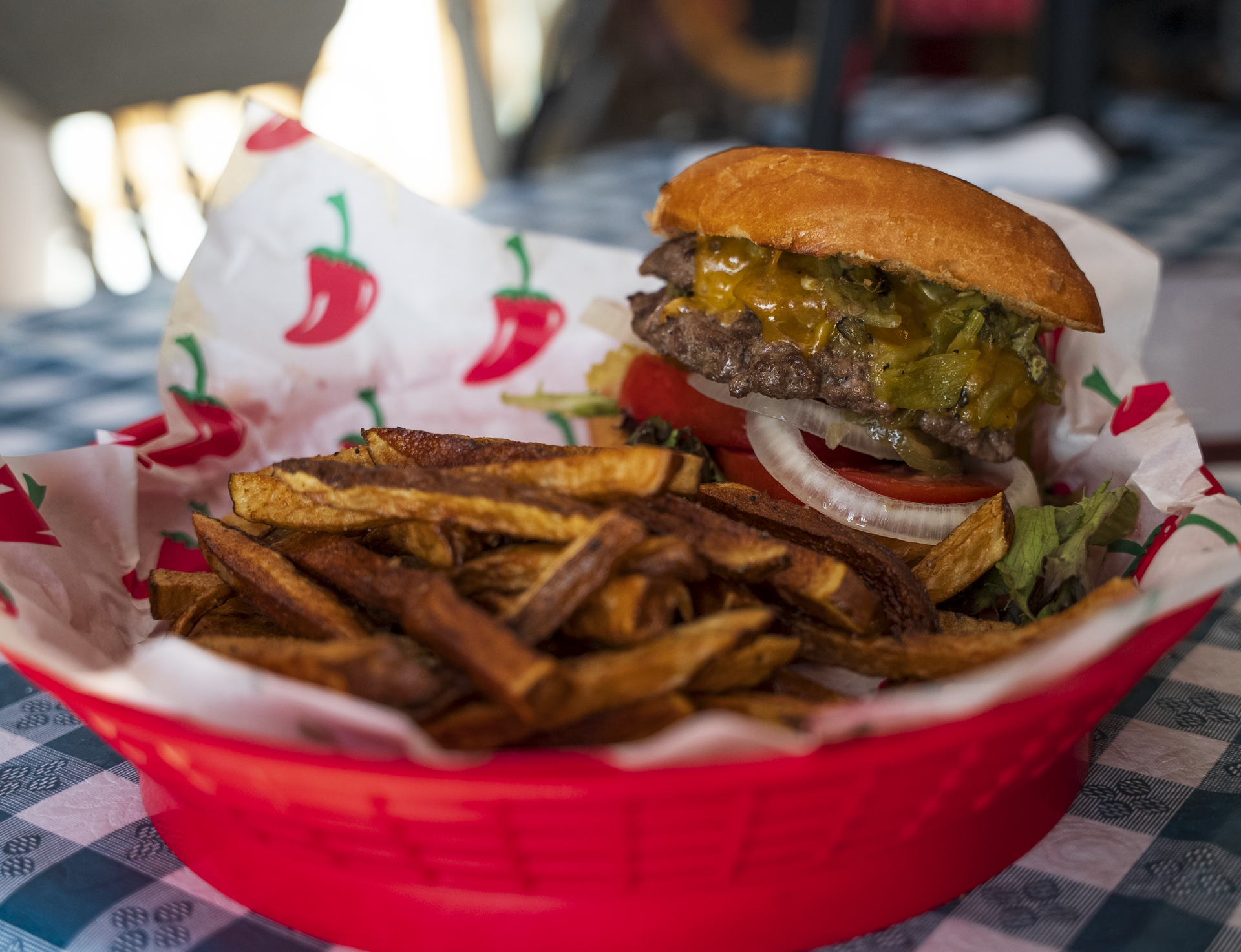Burger and fries in a red basket on a checkered tablecloth, with tomato and lettuce visible