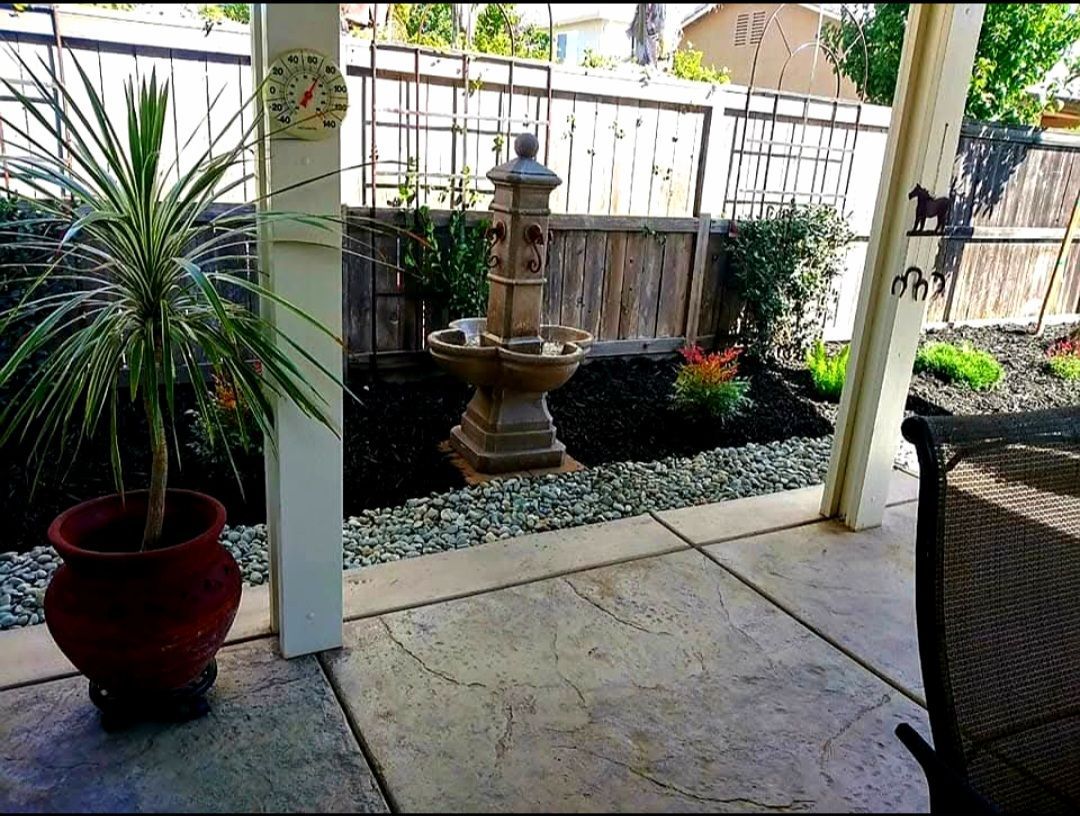 Backyard patio with potted plant, fountain, garden, and gray stone floor.