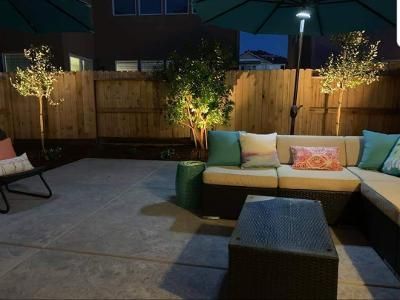 Patio furniture on a stamped concrete patio under a patio umbrella with professional landscape lighting on the trees.