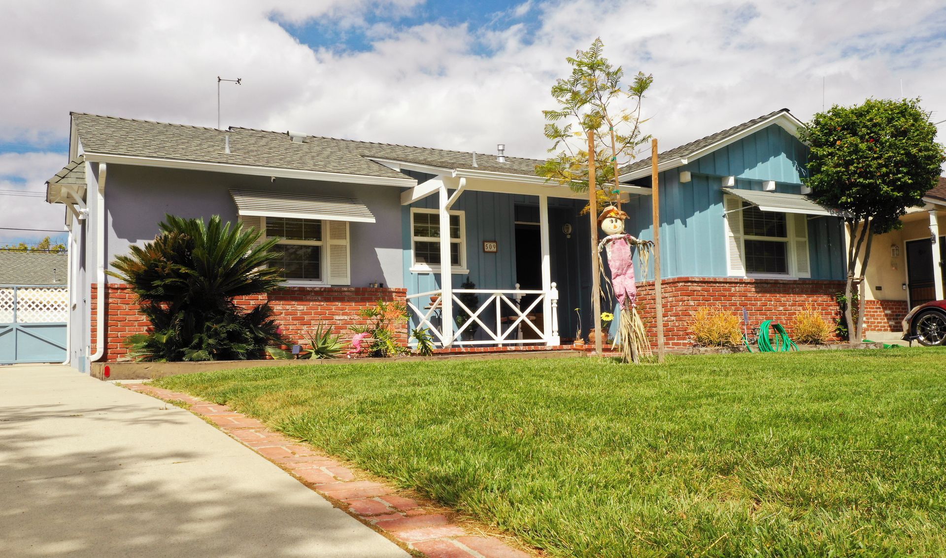 Blue and brick house with a scarecrow in the front yard, sunny day.