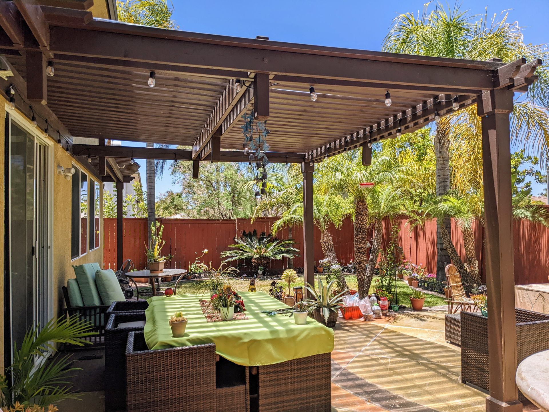 Patio with pergola, table, chairs, and garden in sunny backyard.