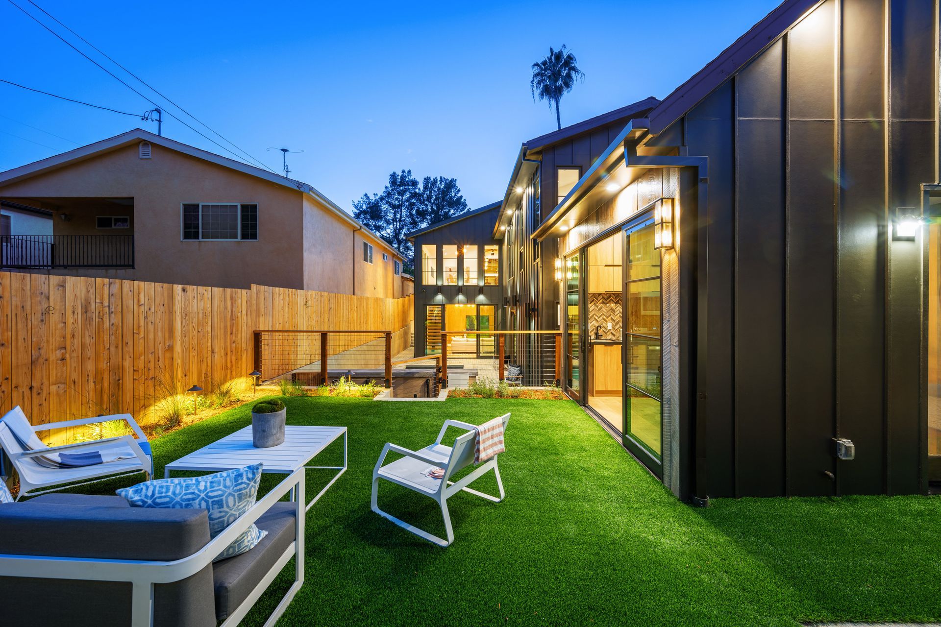 Backyard with patio furniture and green lawn at dusk, next to a modern house.