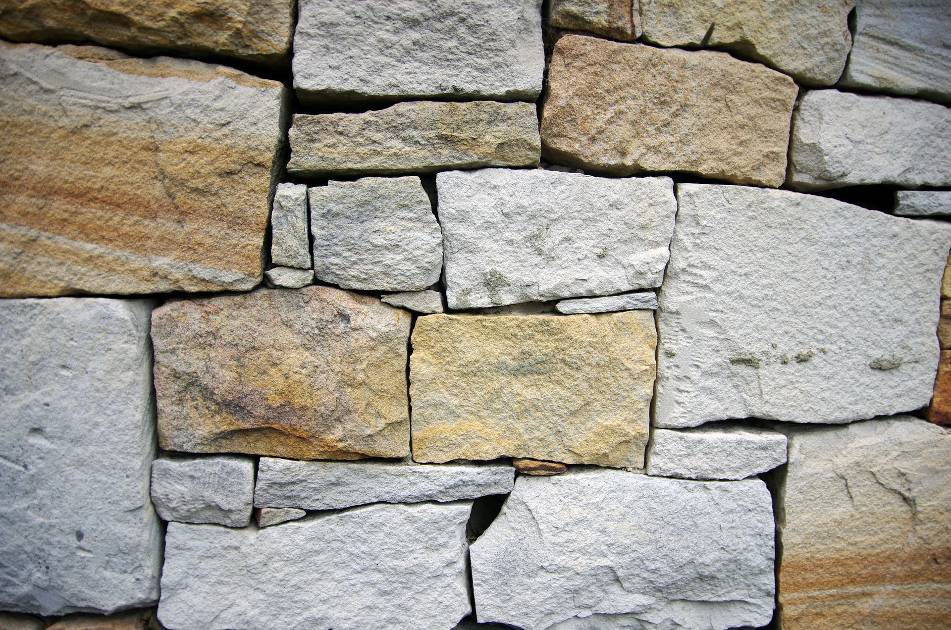 Close-up of a stone wall, featuring rectangular and square-shaped stones in shades of tan, gray, and cream.