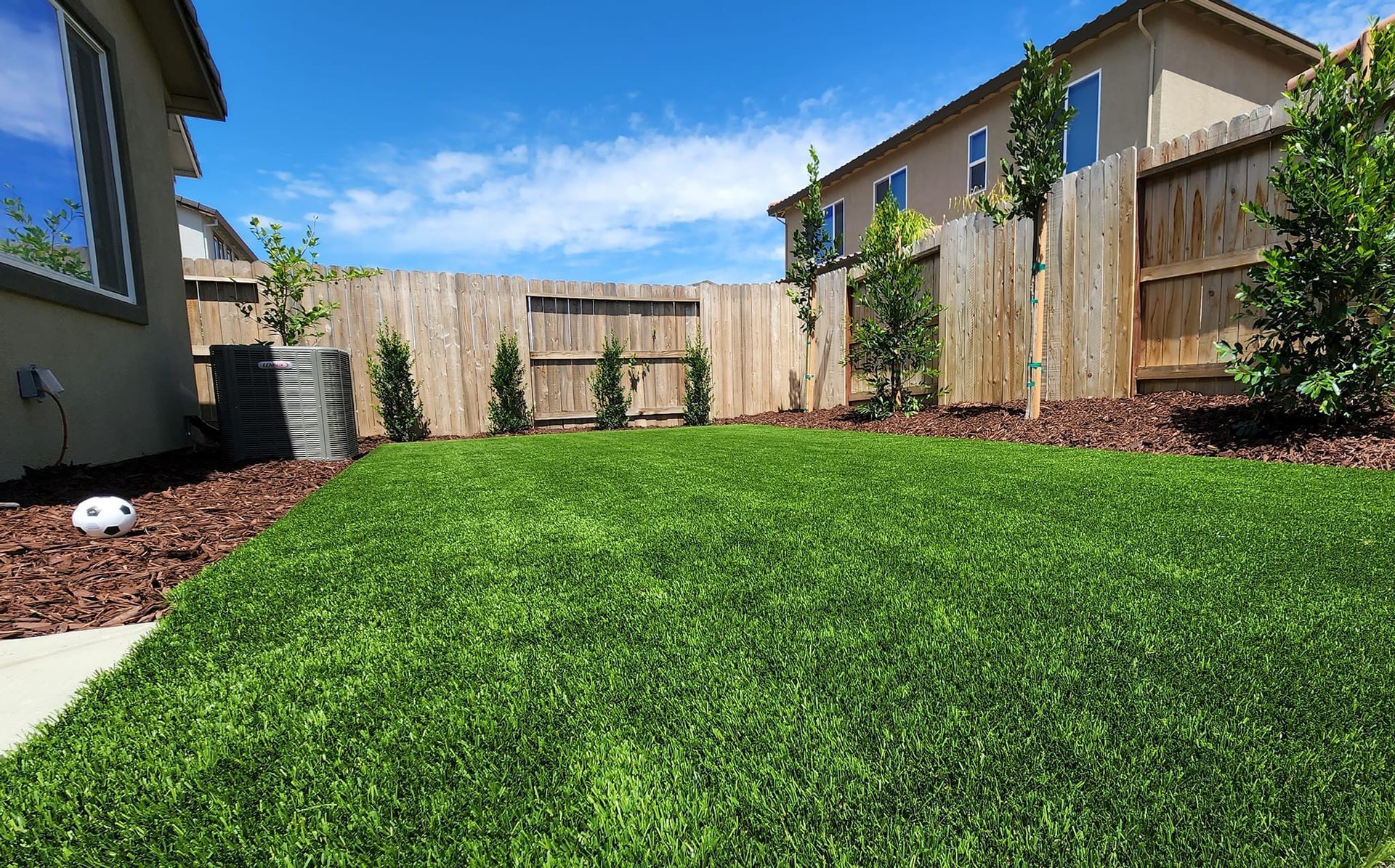 Artificial turf edge next to a red-brown border. Green blades are in sharp focus.