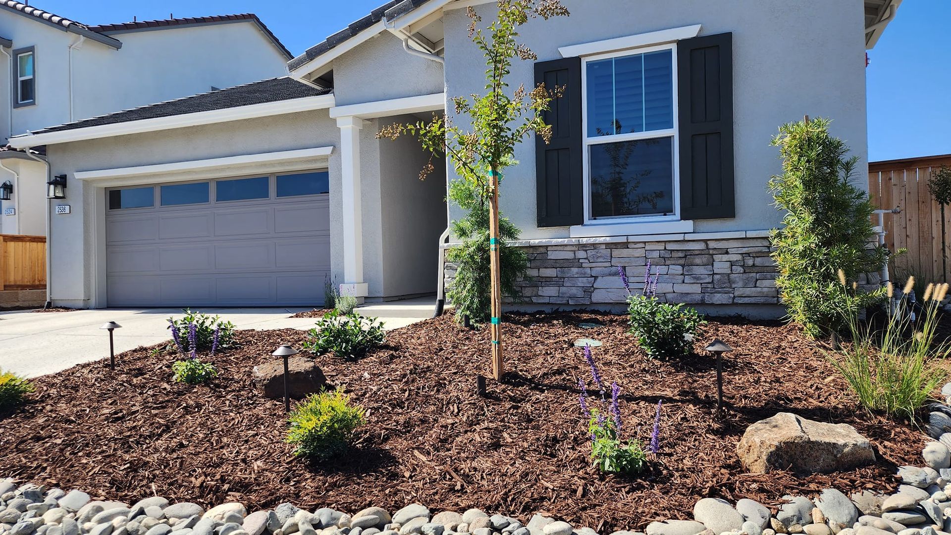 Xeriscape front yard with plants, bark, a dry cobble stream, boulders and landscape lighting.