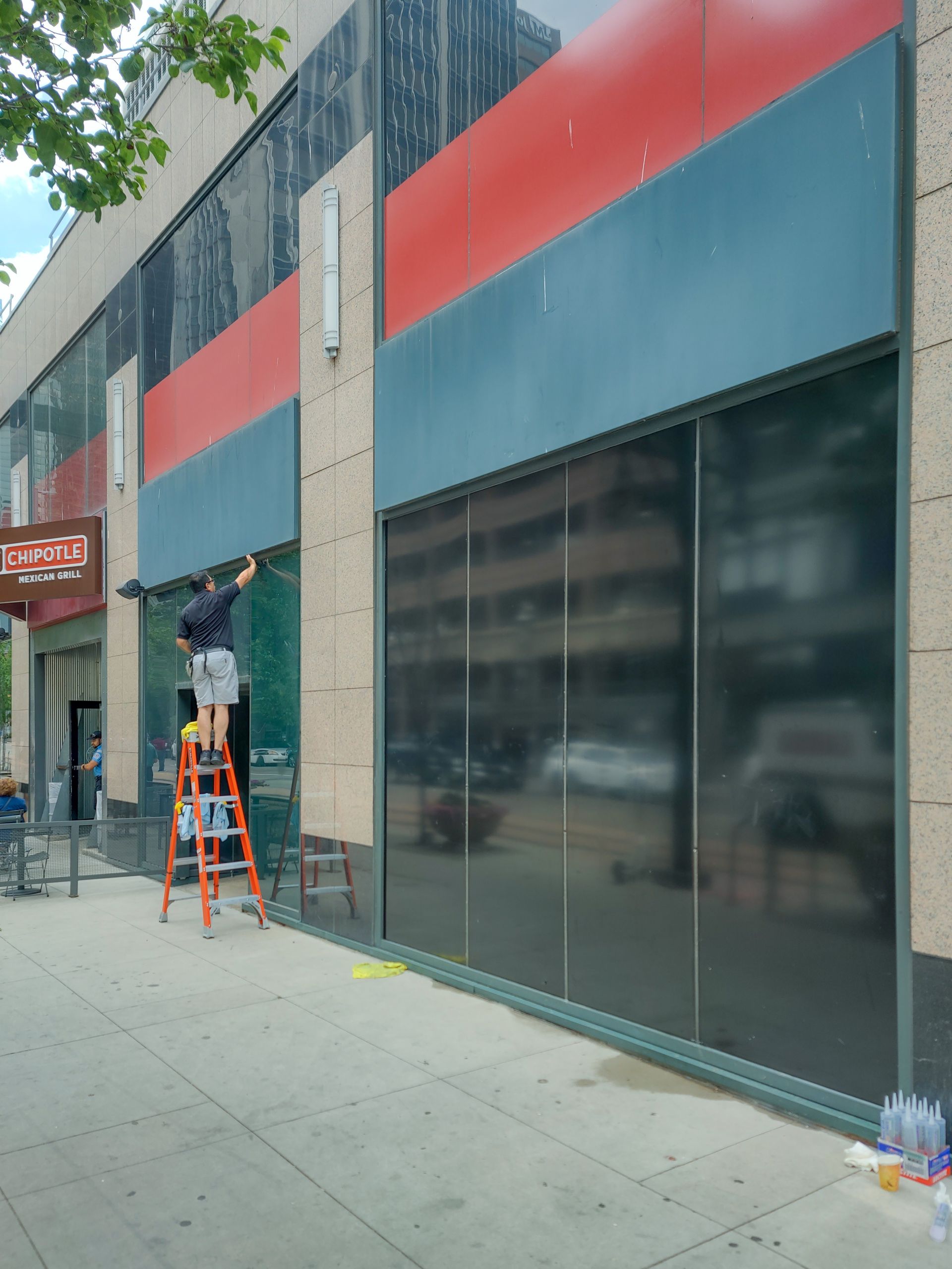 A man on a ladder is tinting the windows of a building