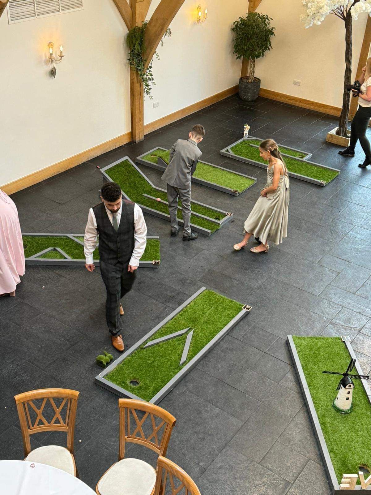 Guests playing mini golf at an indoor event. Several people, including a groom, are on the course.
