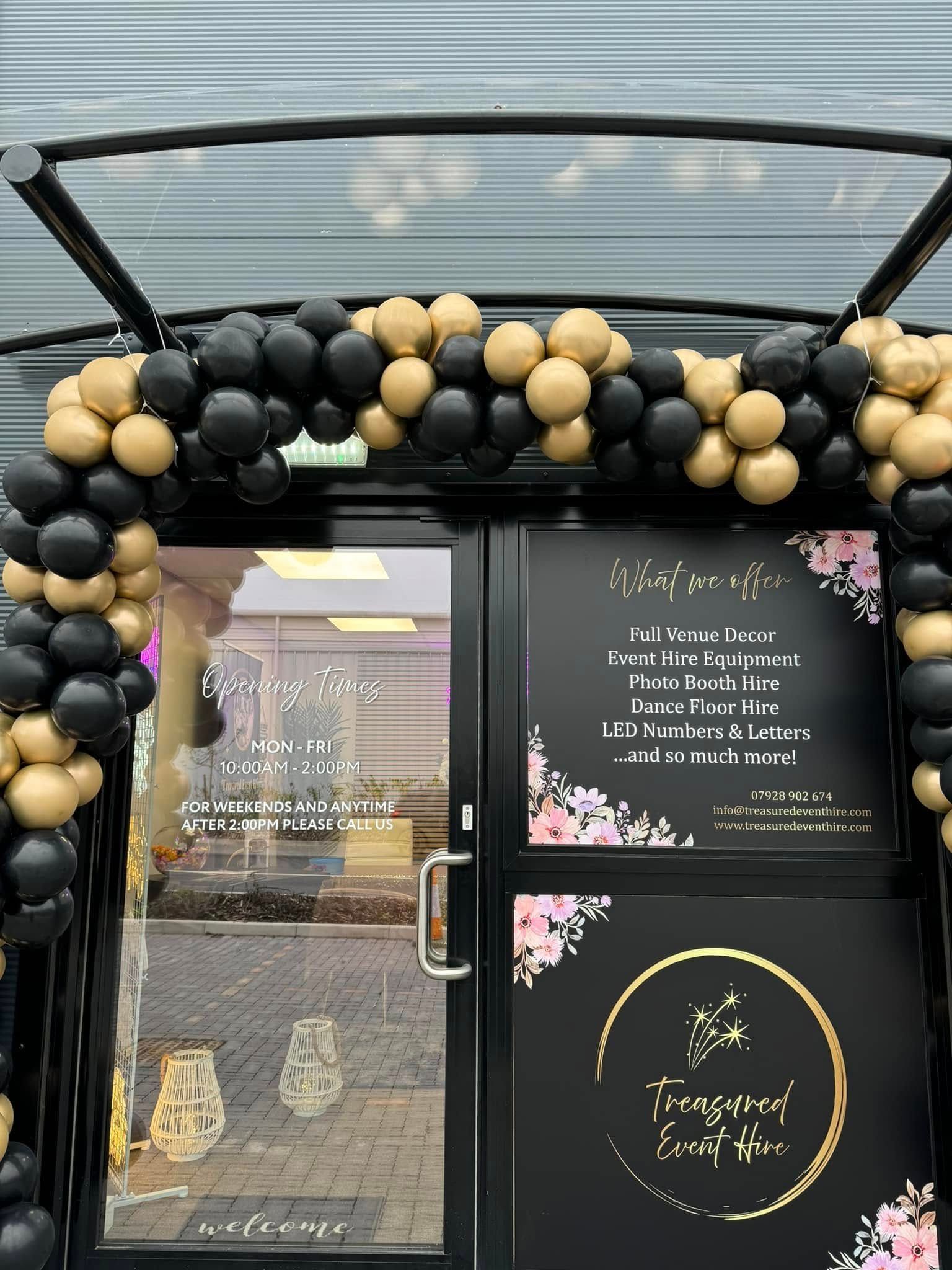 Black and gold balloon arch over a shop entrance with signage; a floral logo is visible.