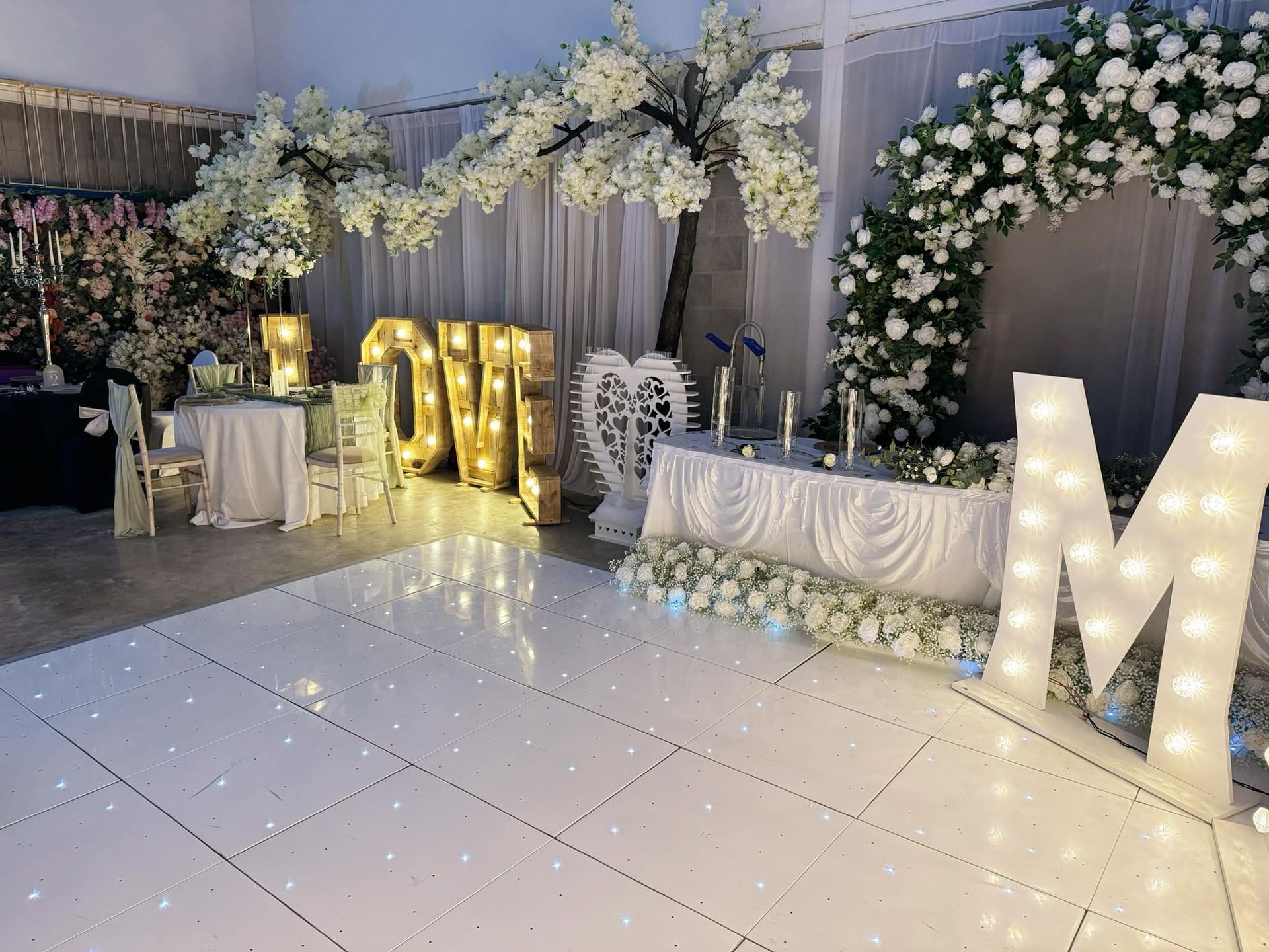 Wedding reception decorated with lights, flowers, and LOVE and M letters.