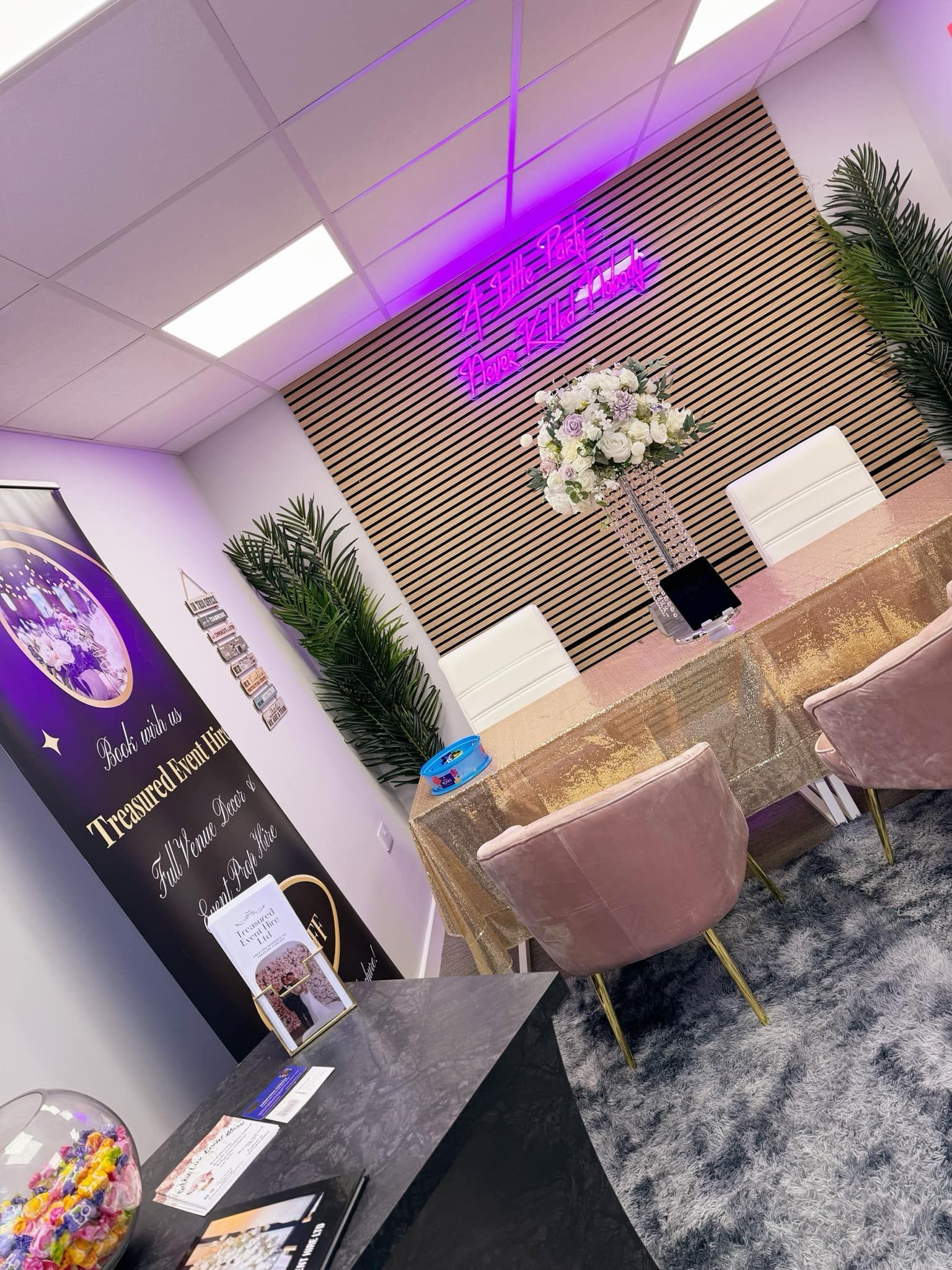 An elegant office with a meeting table, pink chairs, neon sign, and a colorful candy jar.
