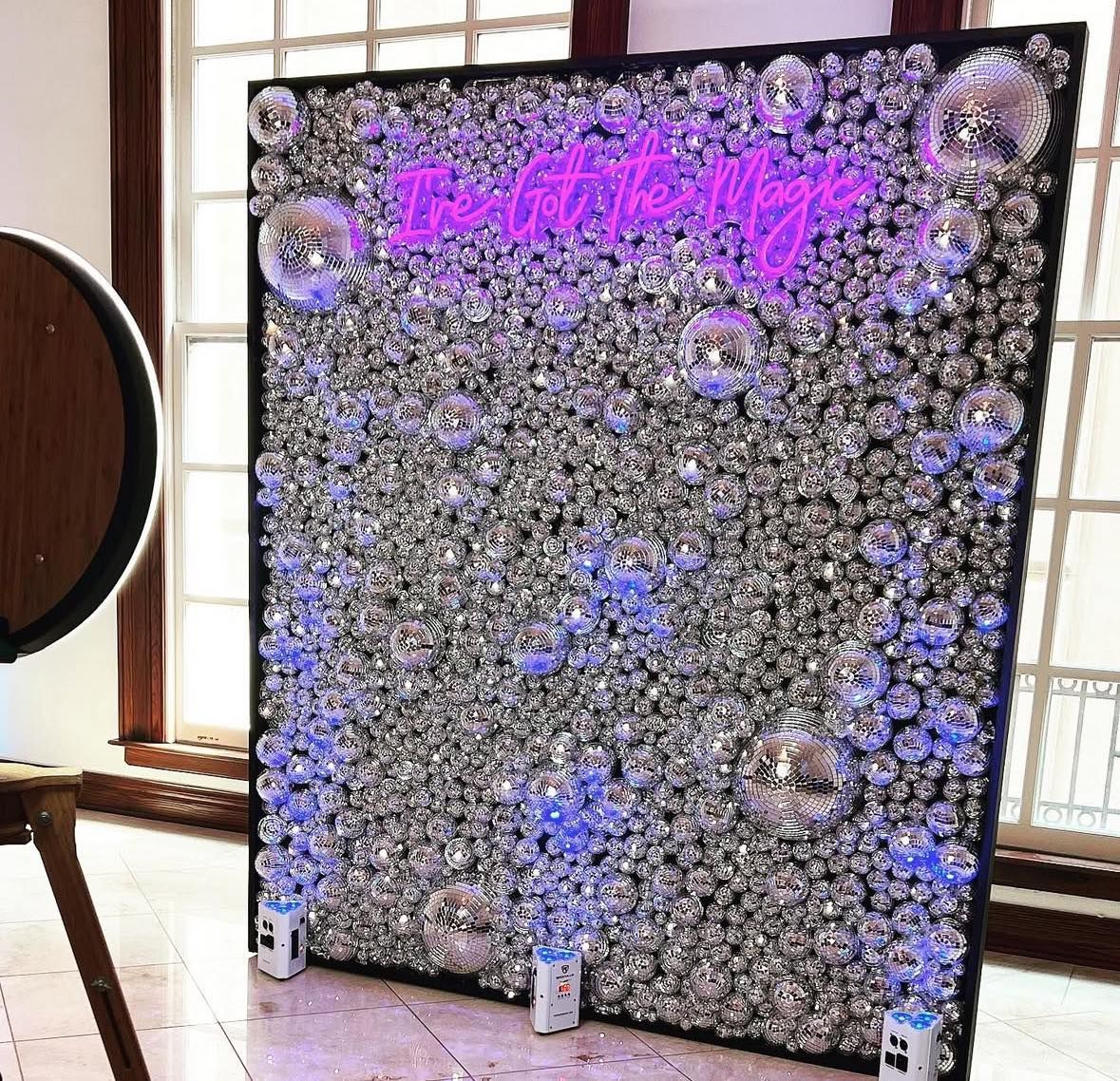 Disco ball photo booth backdrop with neon text and blue lights.