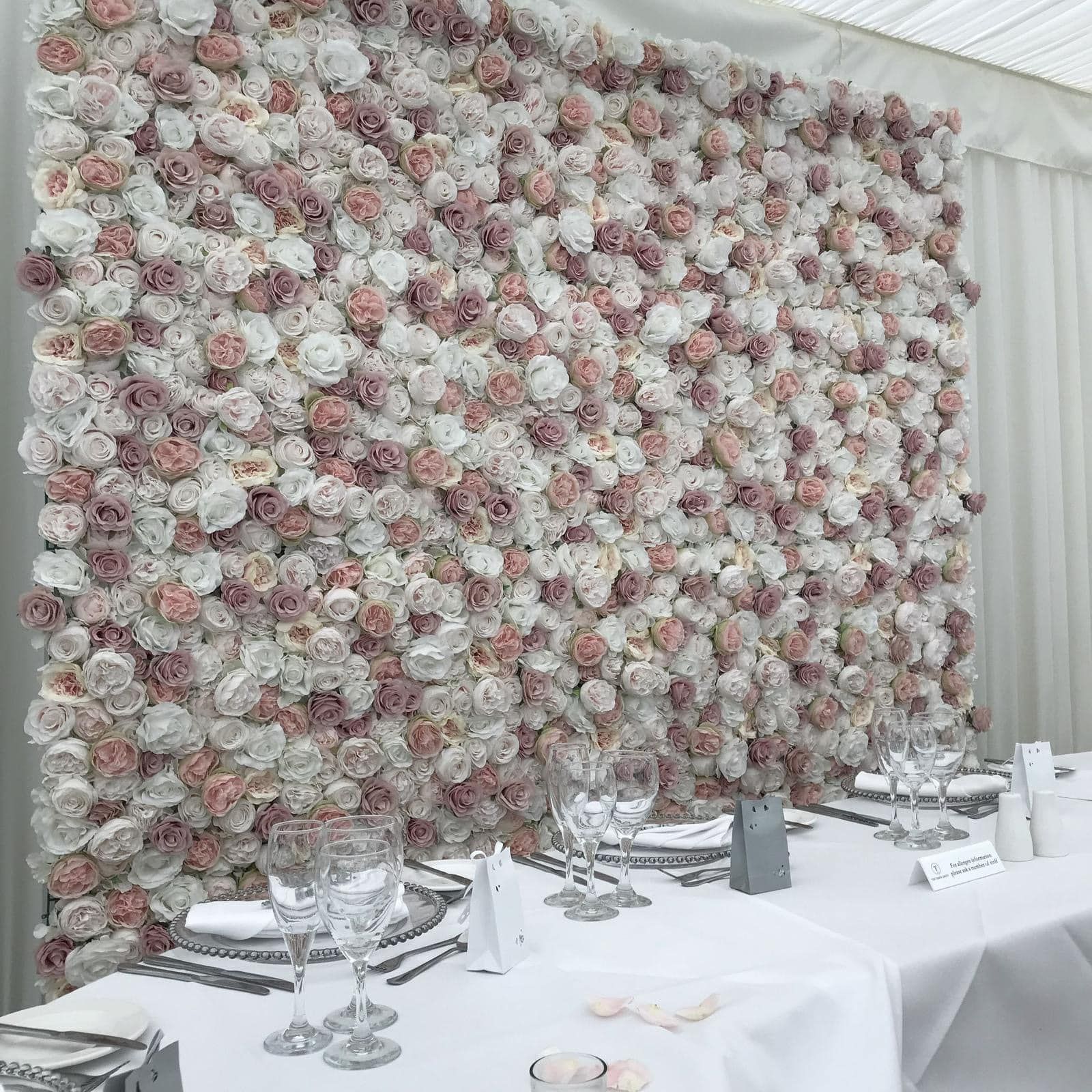 Wedding reception table set with silverware in front of a flower wall of pink and white roses.