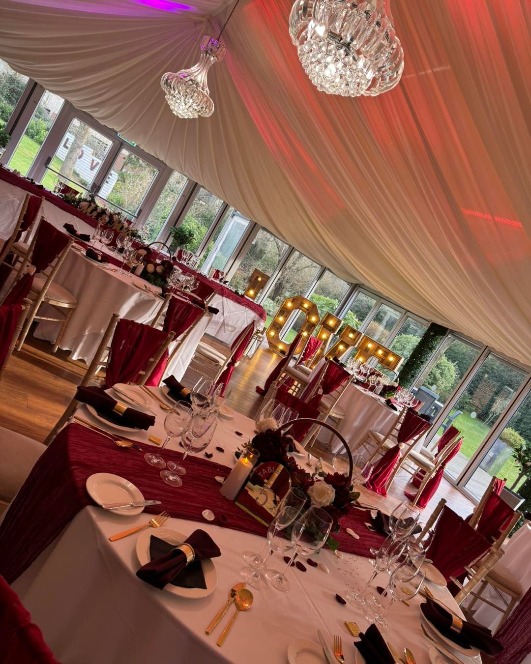 Formal dining setup with burgundy and gold accents, in a light-filled room, with a 