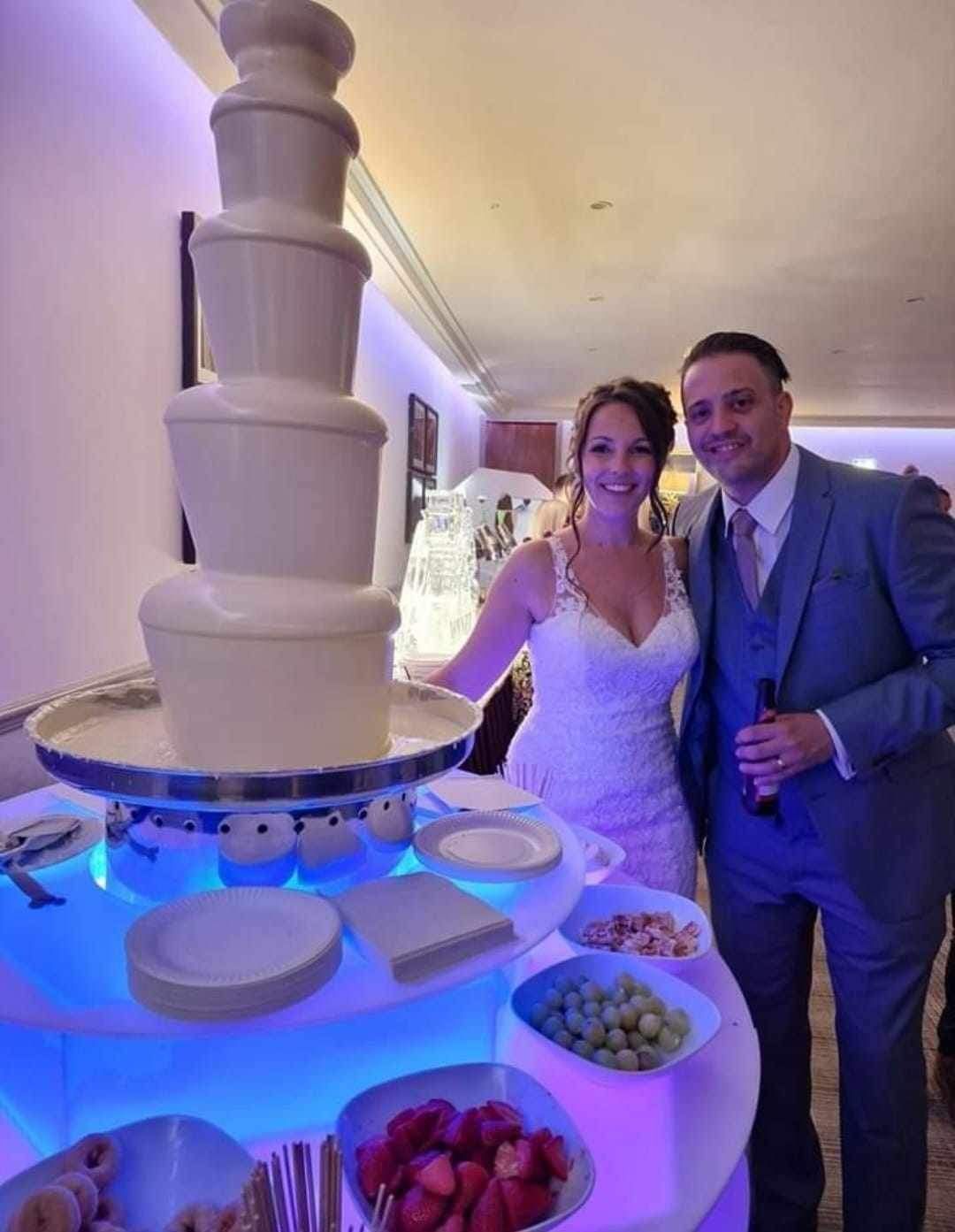 Bride and groom by a white chocolate fountain with snacks at a wedding.