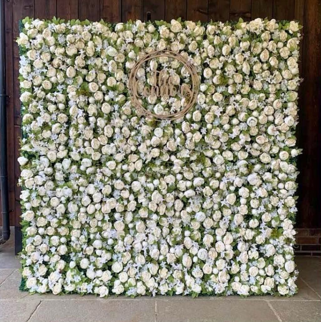 Flower wall with white blooms and a wooden monogram, suitable for weddings.