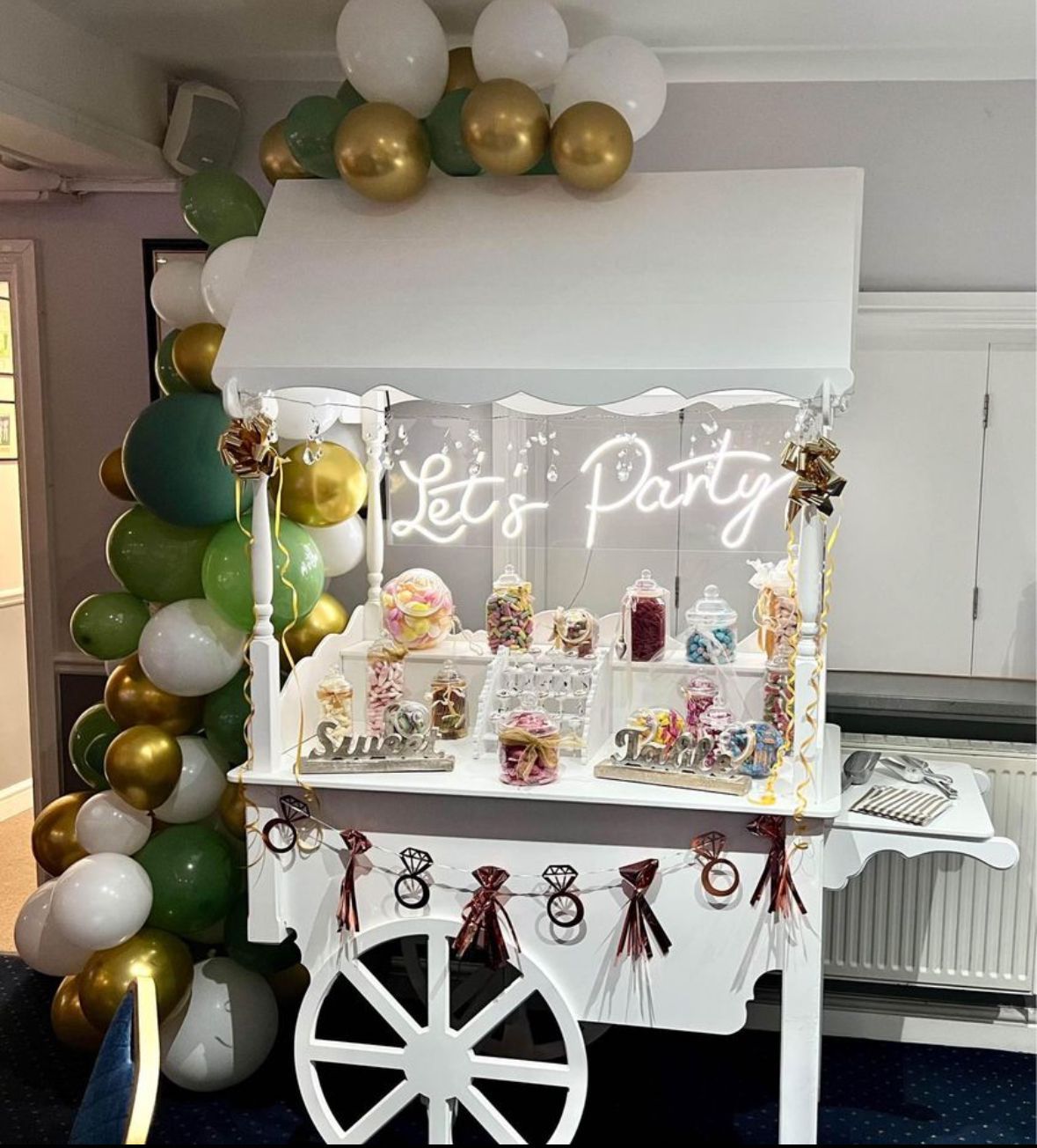 White candy cart decorated with balloons, candy jars, and 