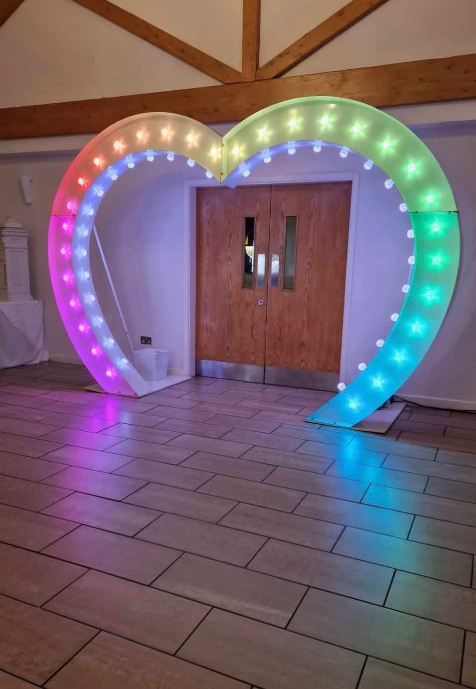 Large, lit heart-shaped archway with colorful lights framing a doorway in a venue.
