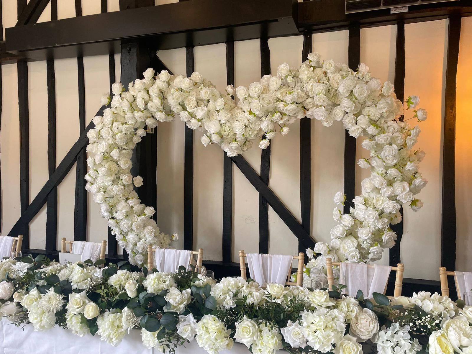 White floral heart over a decorated table with more white flowers, set in a room with dark beams.