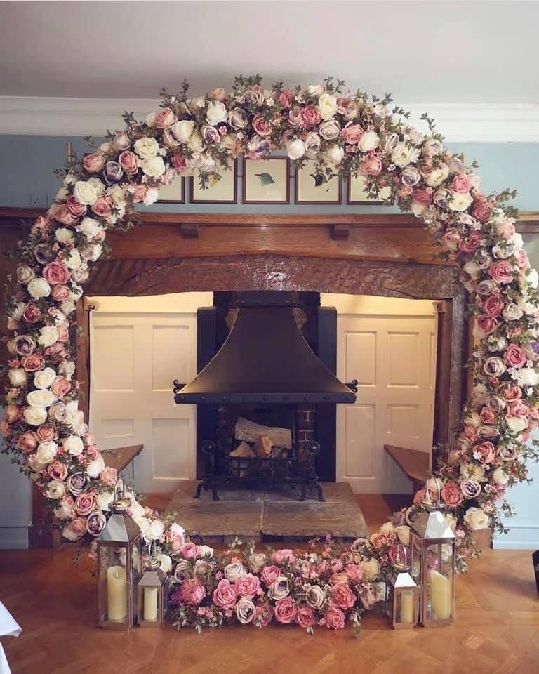 A large floral arch in pink and white decorates a fireplace setting for a wedding.