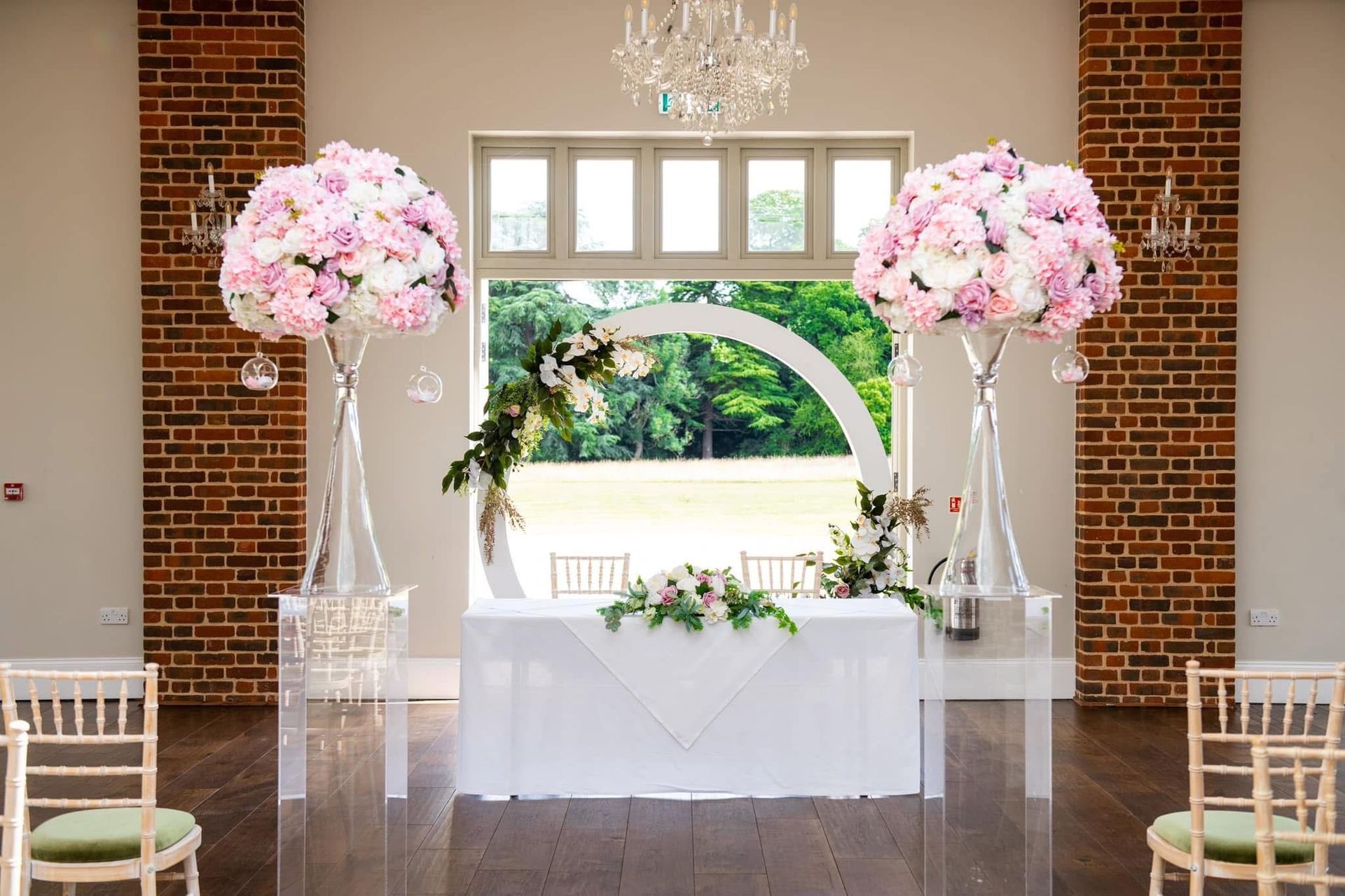 Wedding ceremony setup with pink floral arrangements and a white arch, indoors.