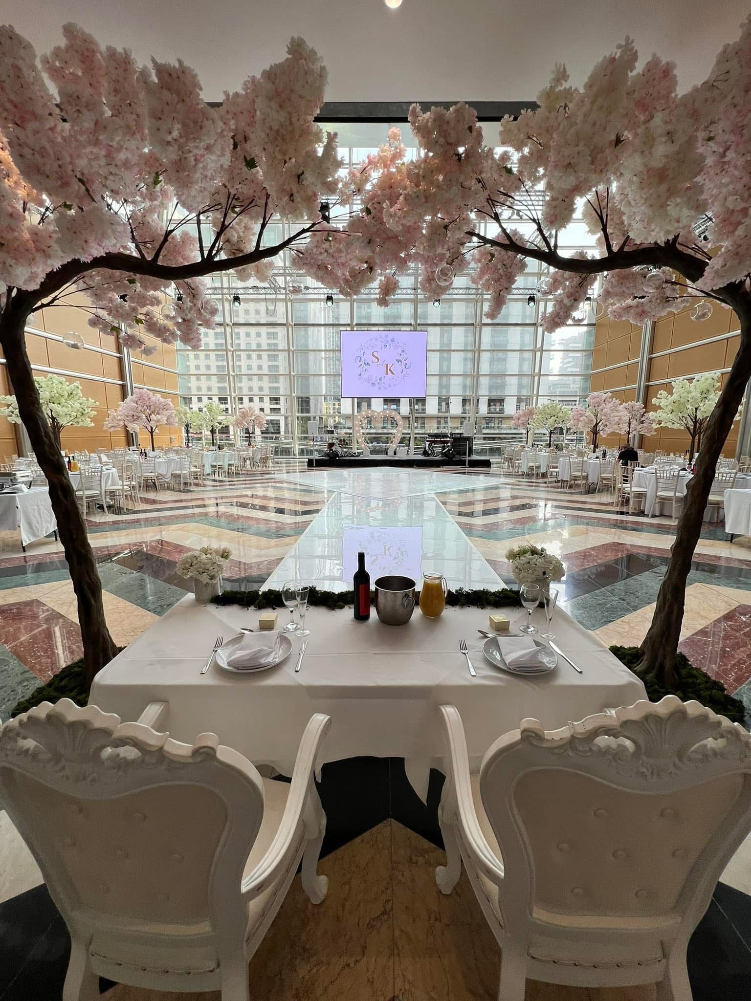 Wedding reception: Bride/groom table with decorative chairs, under cherry blossom trees, overlooking dance floor and guests.