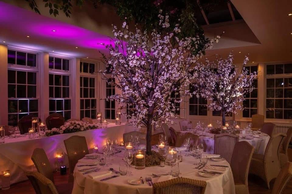 Elegant dining room, round tables set for a formal event, with cherry blossom centerpieces, soft lighting.