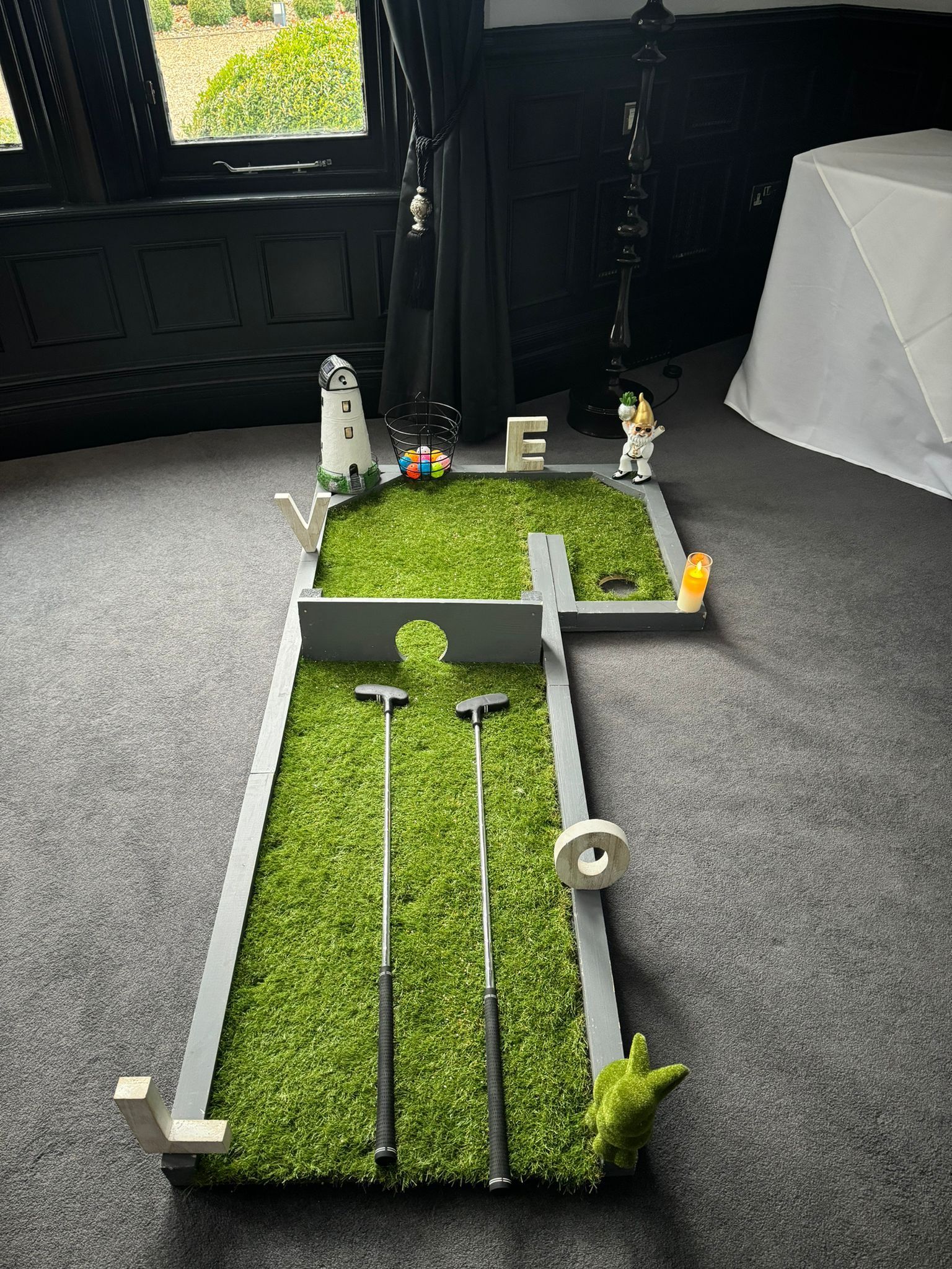 Miniature golf course setup on carpet, with clubs, grass, and decorative elements.