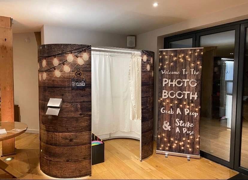 Photo booth with rustic wood paneling, curtain backdrop, and welcome sign.