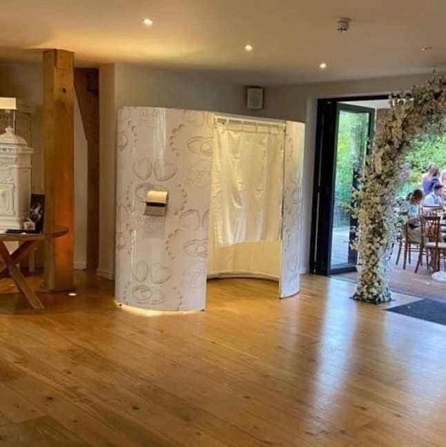 Photo booth in a room with wooden floors, an open door to the outside, and a floral arch.